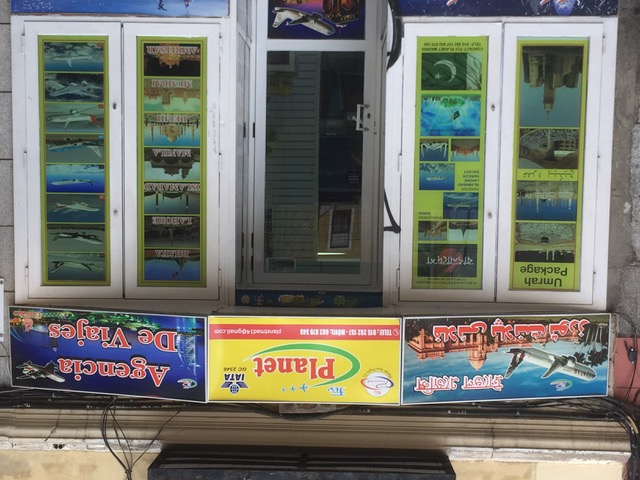 Exterior de una agencia de viajes, analizable como una unidad de paisaje lingüístico de carácter comercial y multilingüe. Podemos distinguir en ella hasta cuatro lenguas diferentes: español (rótulo superior derecha); bengalí (línea superior del rótulo superior izquierda) árabe (línea inferior del rótulo superior izquierda) e inglés (en la expresión “Umrah package”, que se puede leer en la parte superior de la vitrina izquierda). Madrid, barrio de Embajadores, noviembre de 2017. Luis Guerra