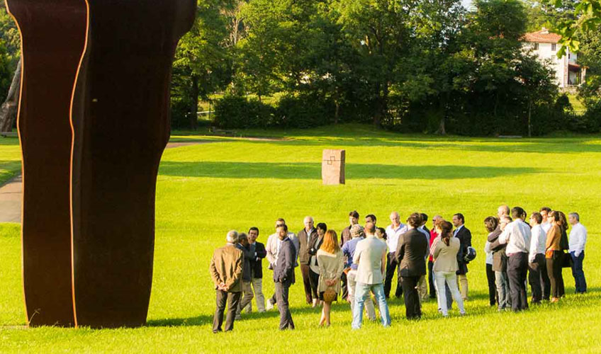 Grupo visitando Chillida Leku bajo la sombra de Buscando la luz I (acero corten, 1997). ©Zabalaga Leku. San Sebastián, VEGAP, 2019. Sucesión Chillida y Hauser & Wirth. Foto Mikel Chillida