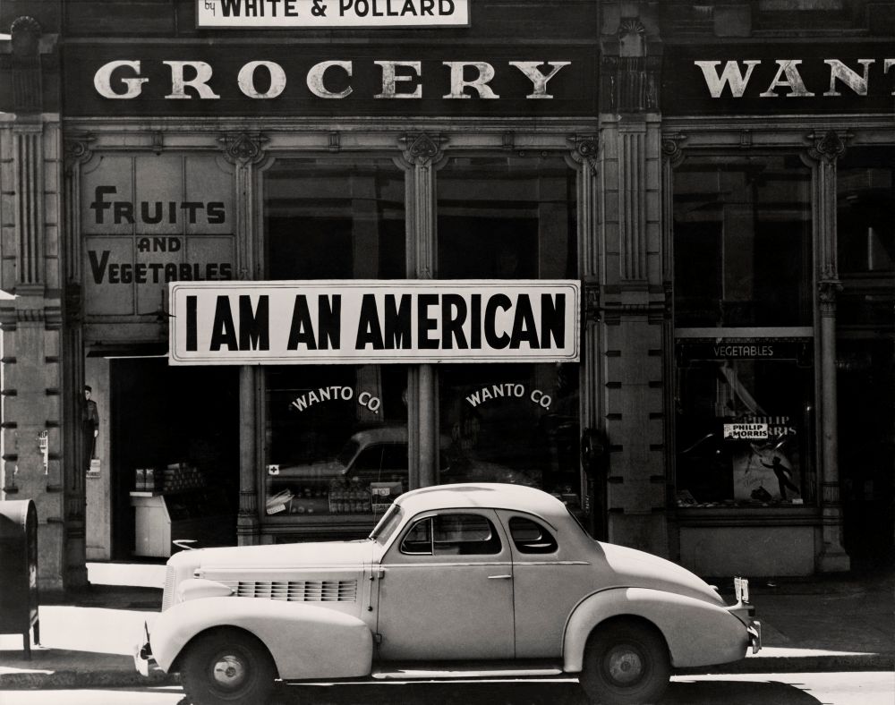 Dorothea Lange. A large sign reading I am an American, 1942. The New York Public Library